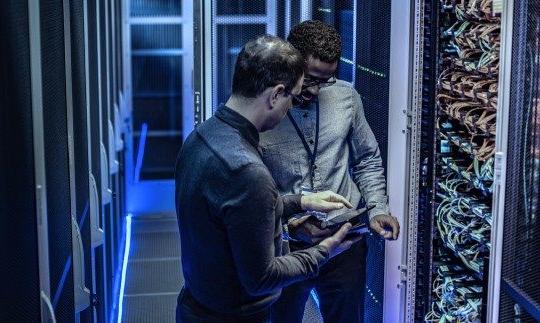 2 men in a server room discussing cybersecurity for government and looking at a tablet